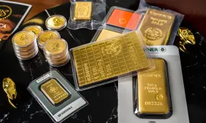 Złote sztabki i monety, w tym 1 gram złota, błyszczą na czarnym tle. Widać też złoty wąż.