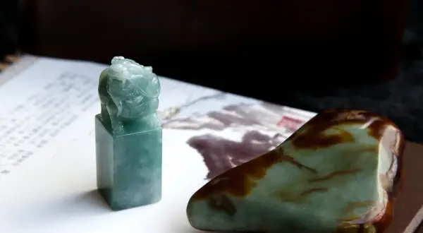 Zielony jadeitowy pieczęć z lwem, obok surowego kamienia. Ten jadeit znak zodiaku symbolizuje siłę i ochronę.