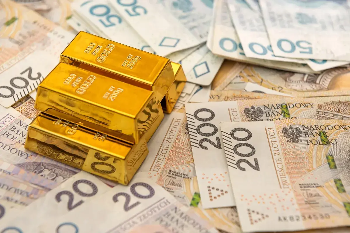 Sztabki złota na tle polskich banknotów. Rozważasz sprzedaż złota? Pamiętaj o podatku!