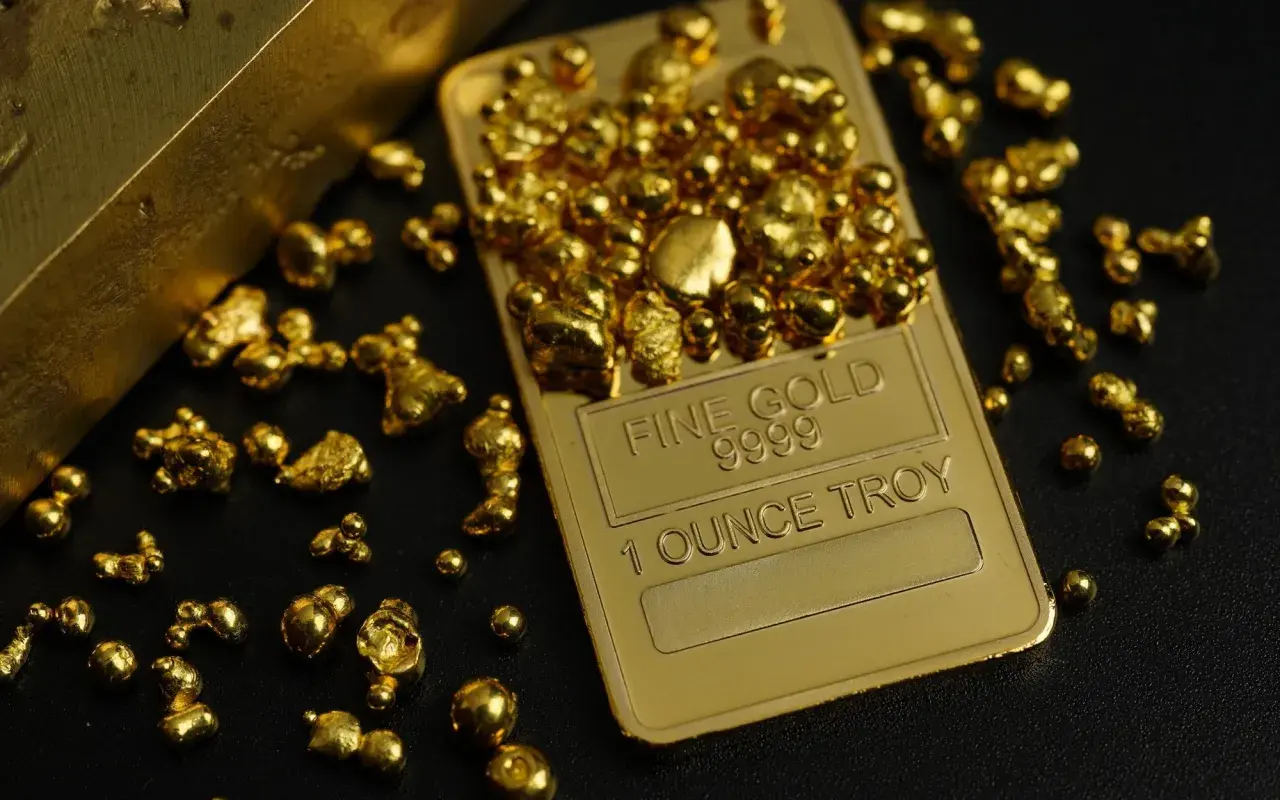 Sztabka "Fine Gold 9999 1 OUNCE TROY" otoczona złotymi samorodkami. Wizualizacja inwestycji w złoto.