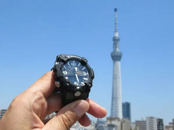Zegar sterowany radiowo jak działa? W tle Tokyo Skytree, ręka trzyma zegarek G-Shock, który synchronizuje się z sygnałem radiowym.