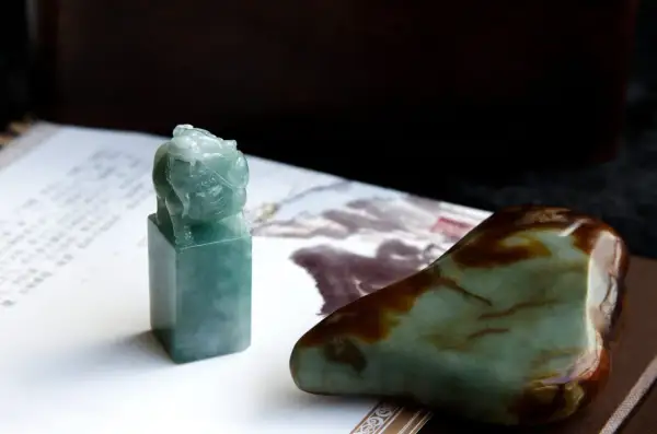 Zielony jadeitowy pieczęć z lwem, obok surowego kamienia. Ten jadeit znak zodiaku symbolizuje siłę i ochronę.
